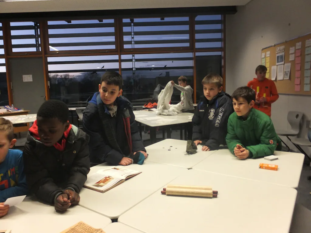 Kinder arbeiten mit Teigrolle und Material an Tischen.